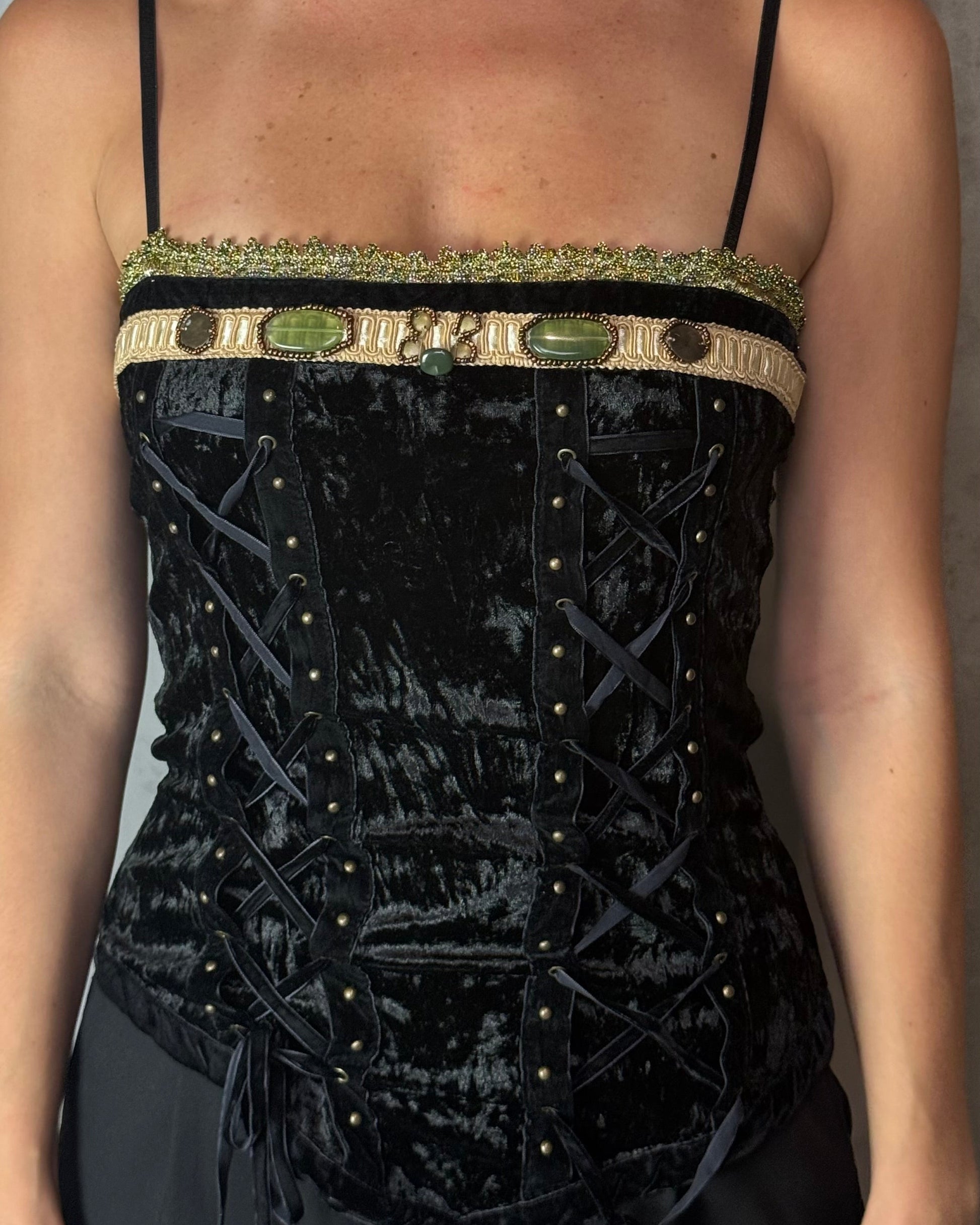 Woman wearing a black velvet corset with gold trim against a plain background
