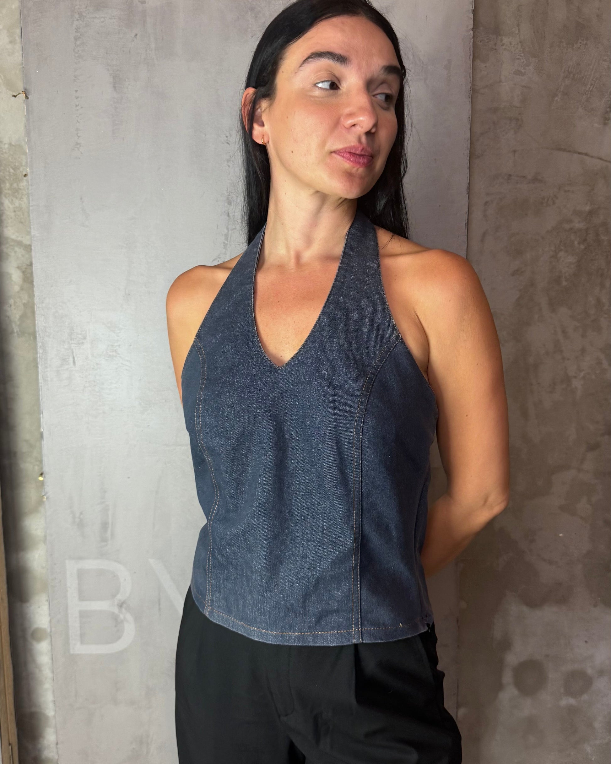 Woman wearing a dark blue sleeveless top and black pants against a gray concrete wall.