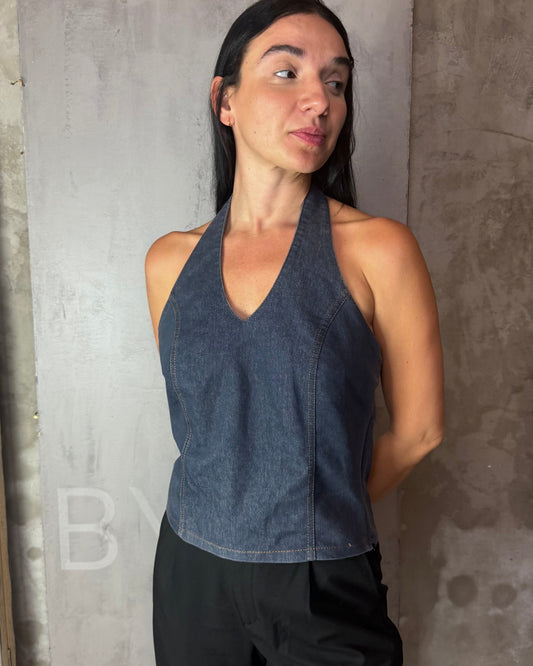 Woman wearing a dark blue sleeveless top and black pants against a gray concrete wall.