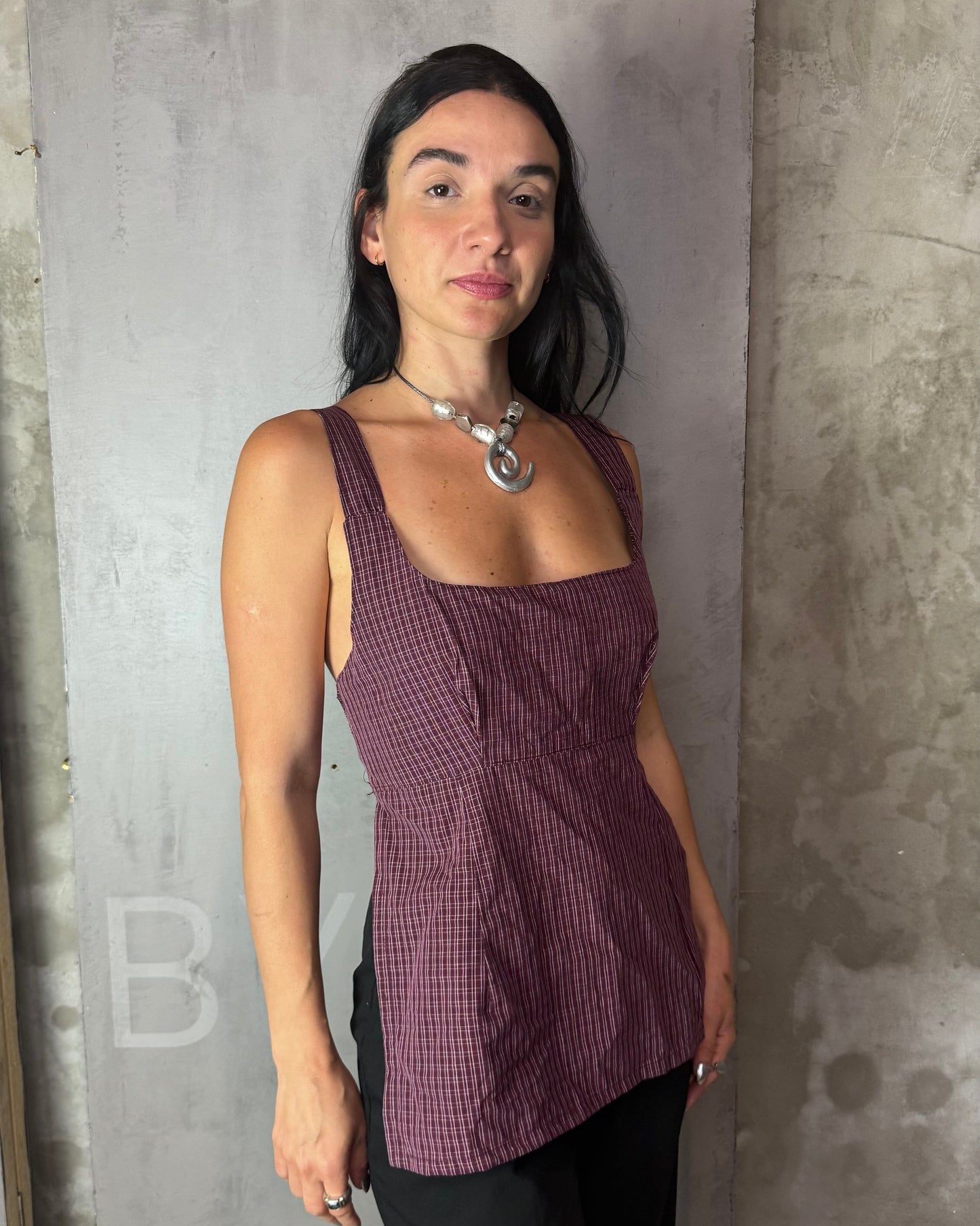 Woman wearing a purple checkered top against a gray concrete wall.