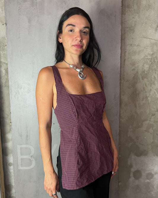 Woman wearing a purple checkered top against a gray concrete wall.