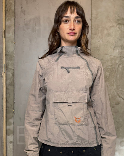 Person wearing a beige jacket with a brand logo against a gray wall