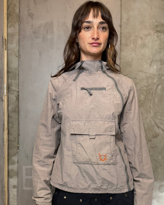 Person wearing a beige jacket with a brand logo against a gray wall